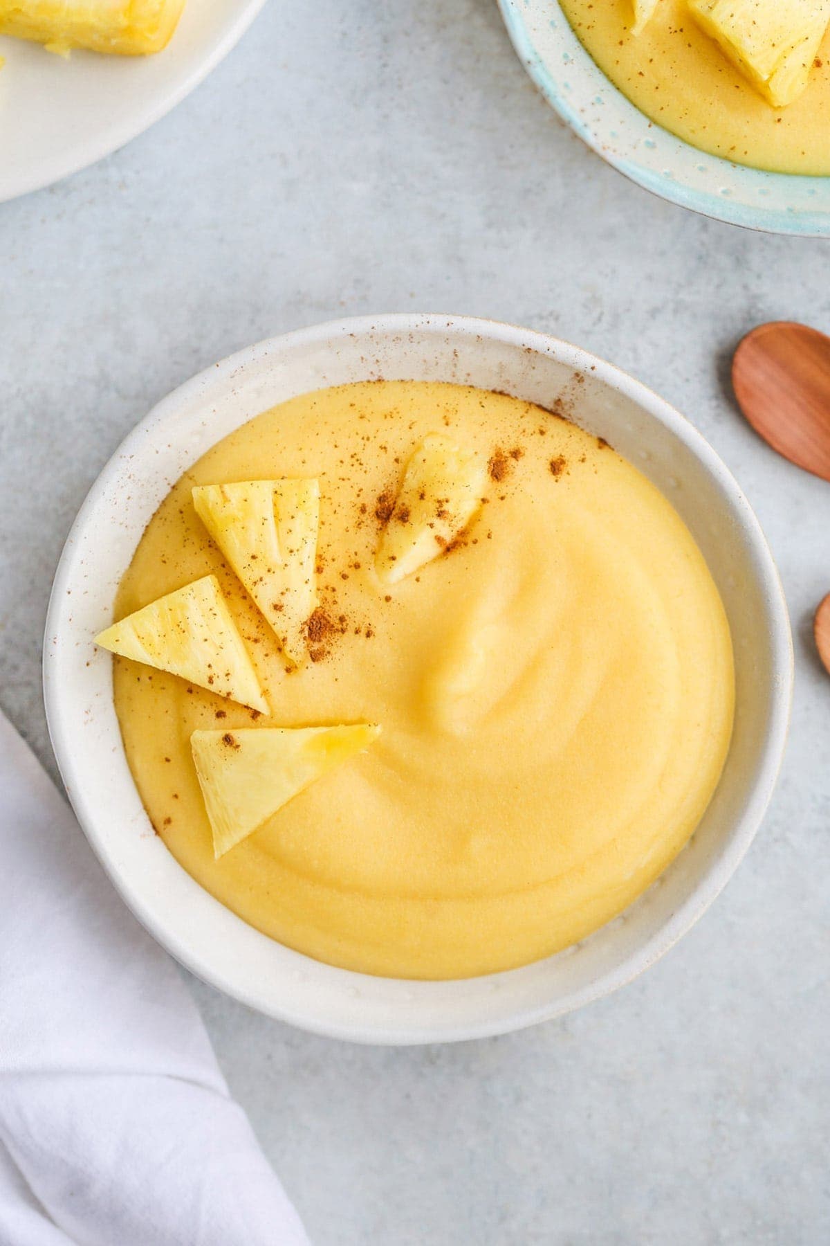 Cornmeal Porridge in a white bowl, with pineapple chunks, and a sprinkle of ground cinnamon