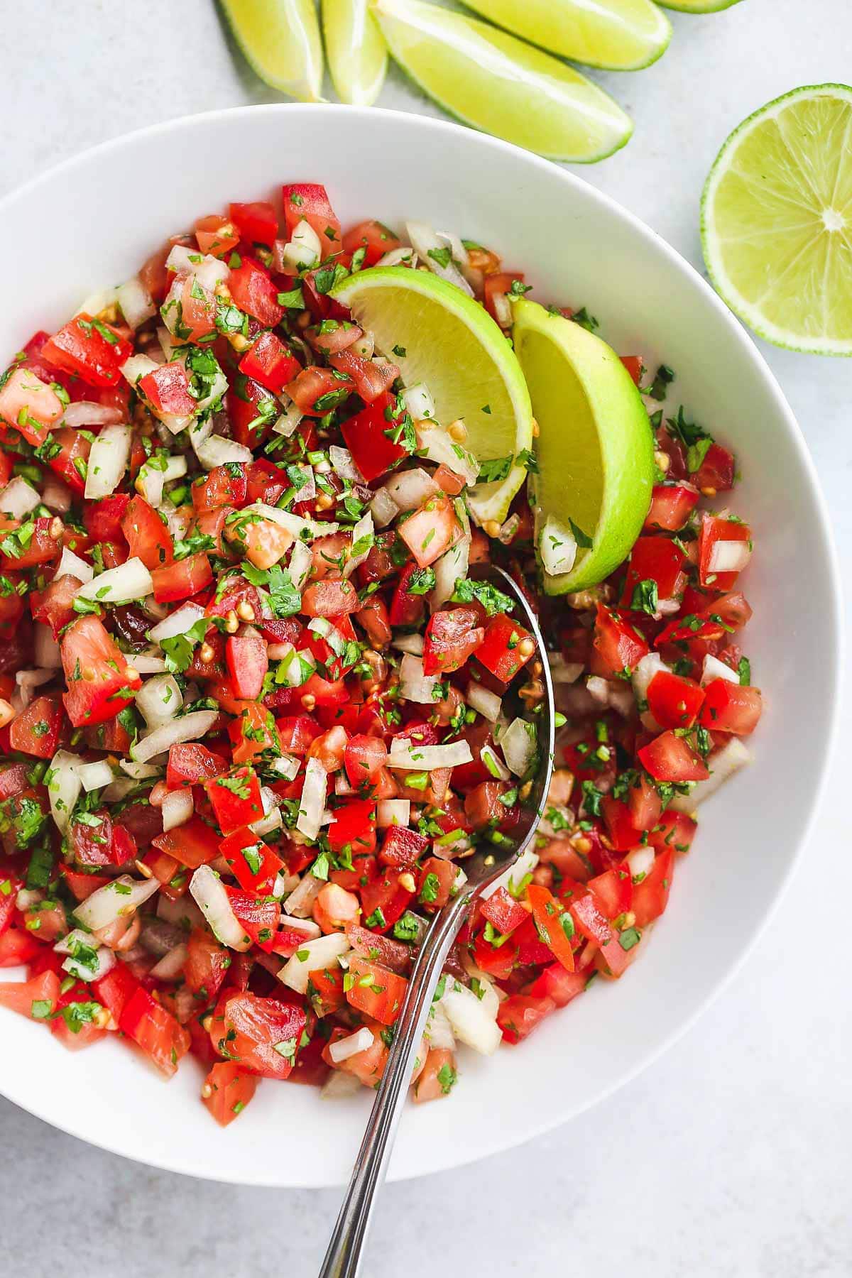 Pico De Gallo Salsa in a white bowl with a serving spoon and lime wedges