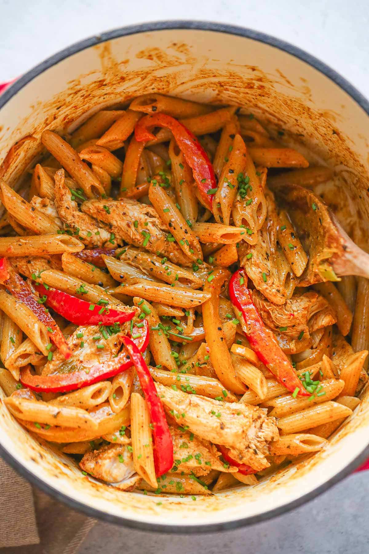 Delicious Rasta Pasta with chicken in a cast iron pot, garnish with chopped chives.