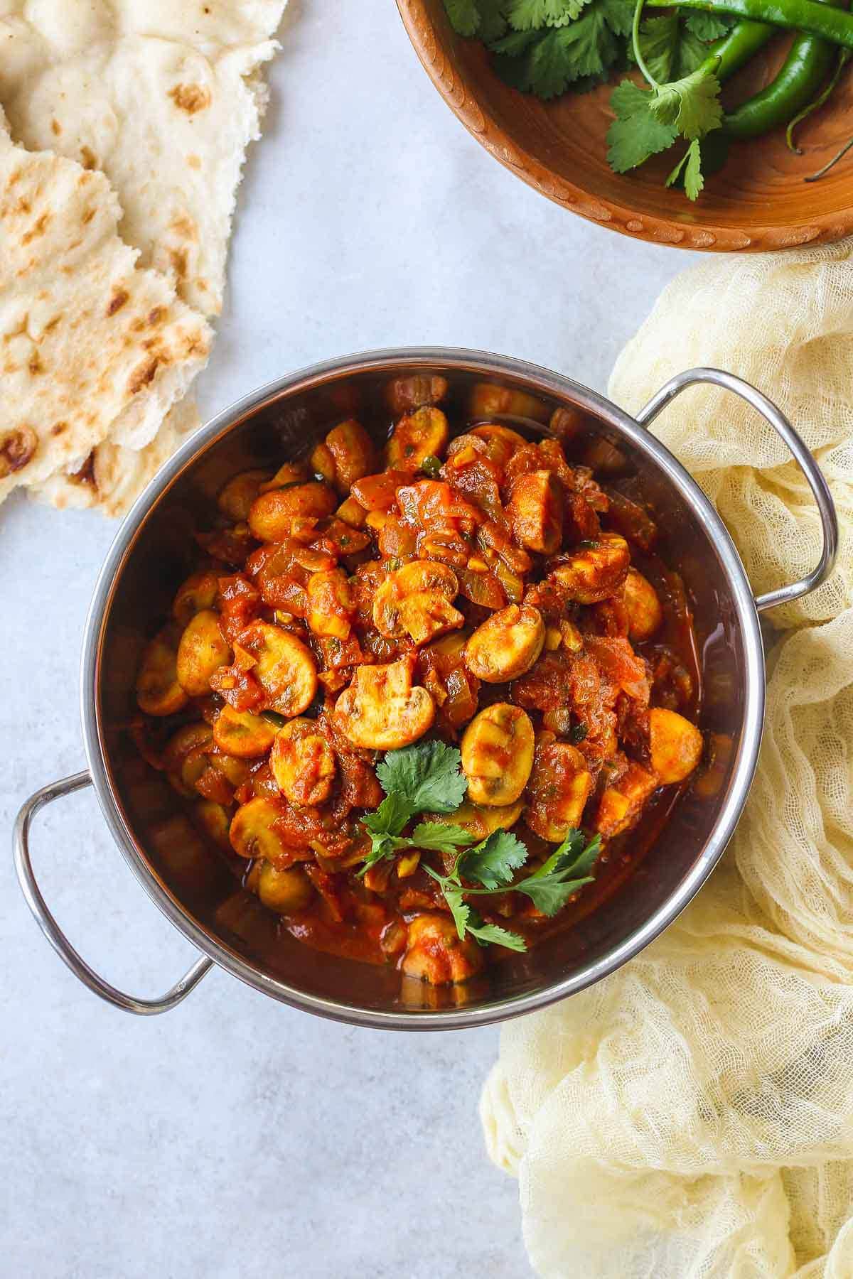 Mushroom Bhaji served in a stainless steel baltic dish, with naan bread on the side.