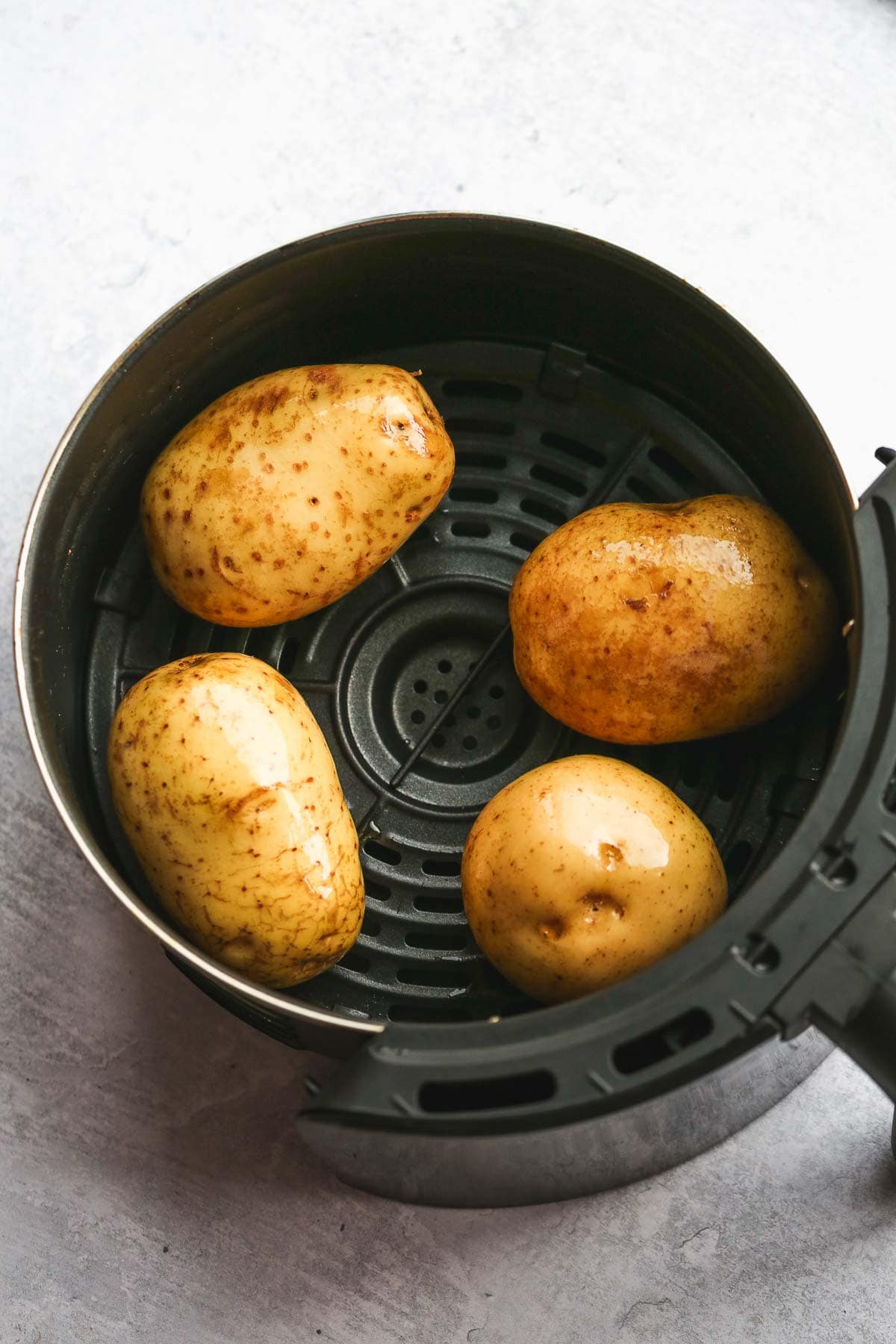 Four raw potatoes in an air fryer basket.