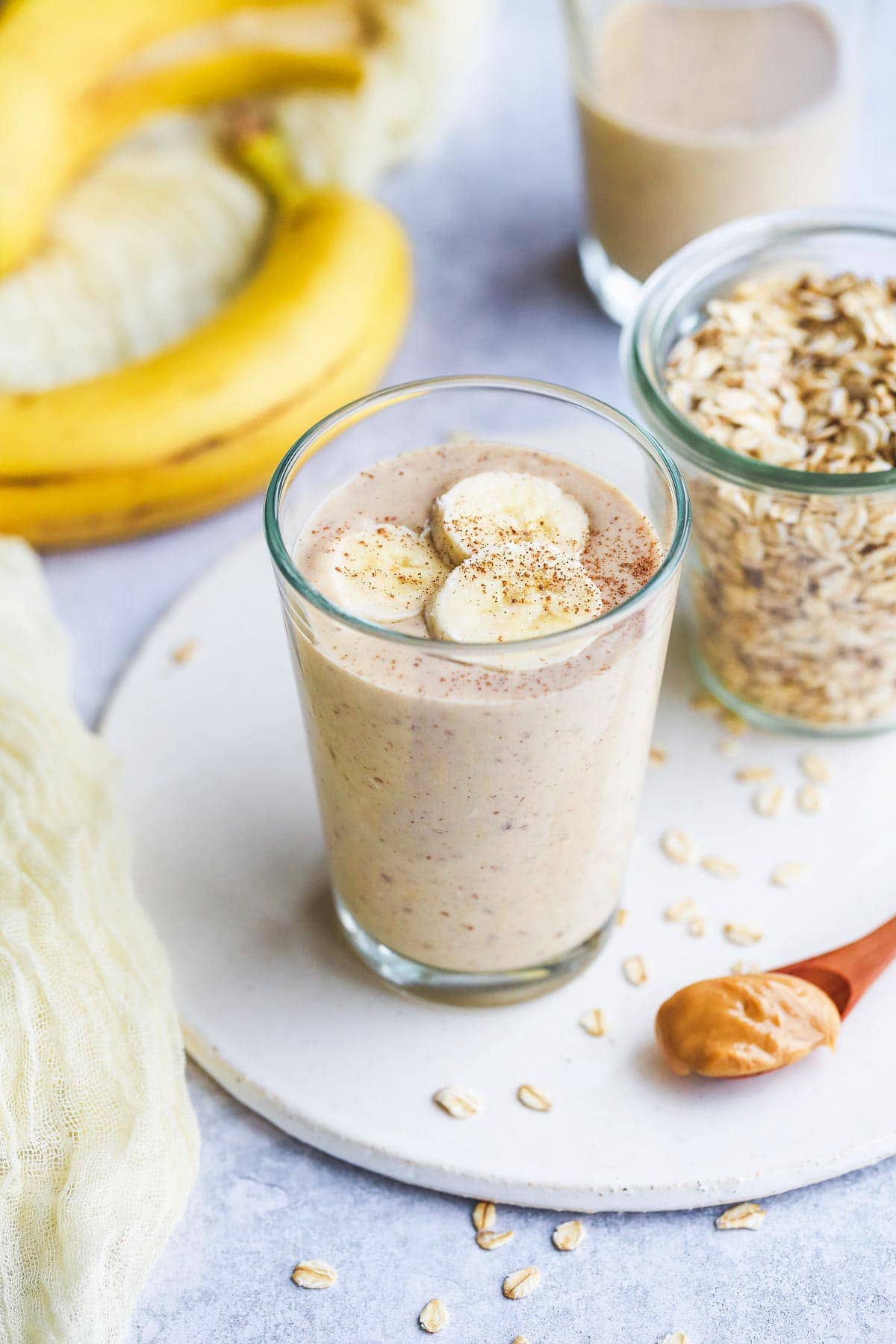 Banana oatmeal smoothie in a glass on a white tray and a teaspoon of peanut butter