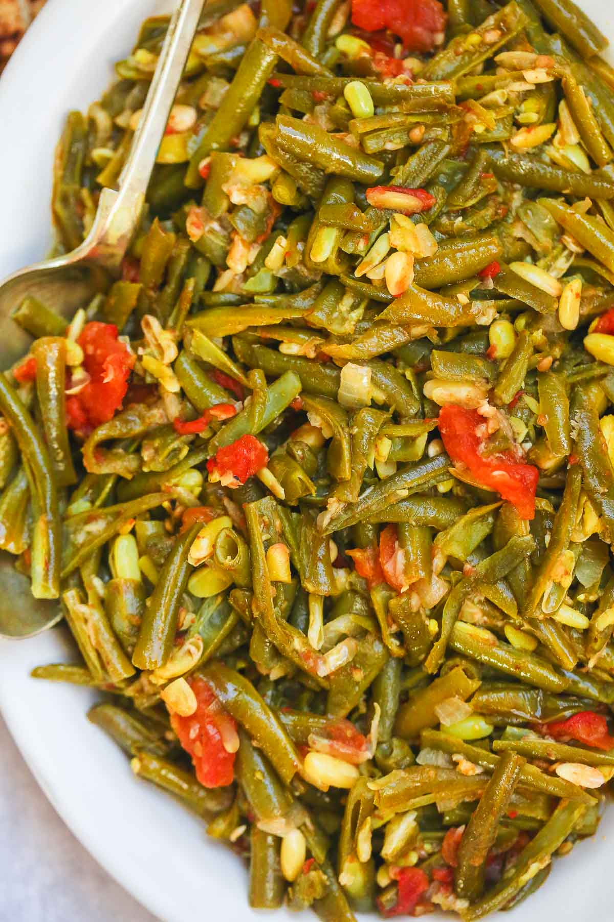 Stewed green beans on a large serving plate and a serving spoon