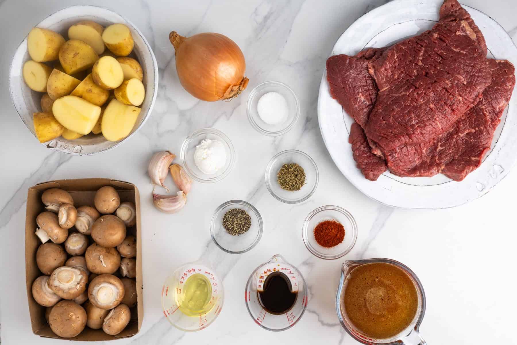 Ingredients for Instant Pot cube steak, including cube steaks, baby potatoes, cremini mushrooms, onion, garlic, beef broth, and seasonings.