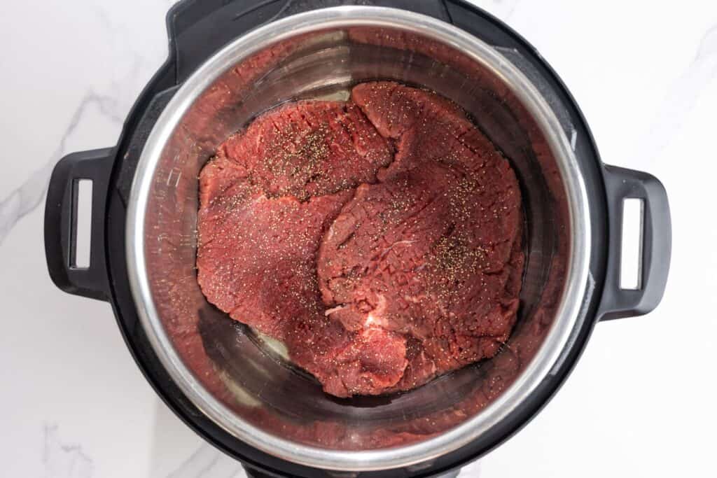 Seasoned cube steaks layered in a 6 quart Instant Pot.