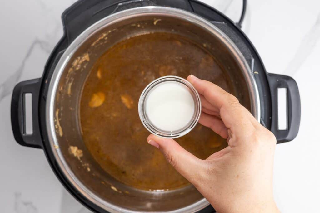Cornstarch slurry being added to the cooking liquid in the Instant Pot to thicken the gravy.