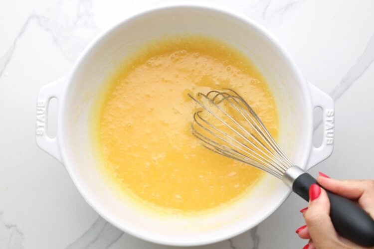 Wet ingredients mixed in a white bowl and a hand holding a whisk