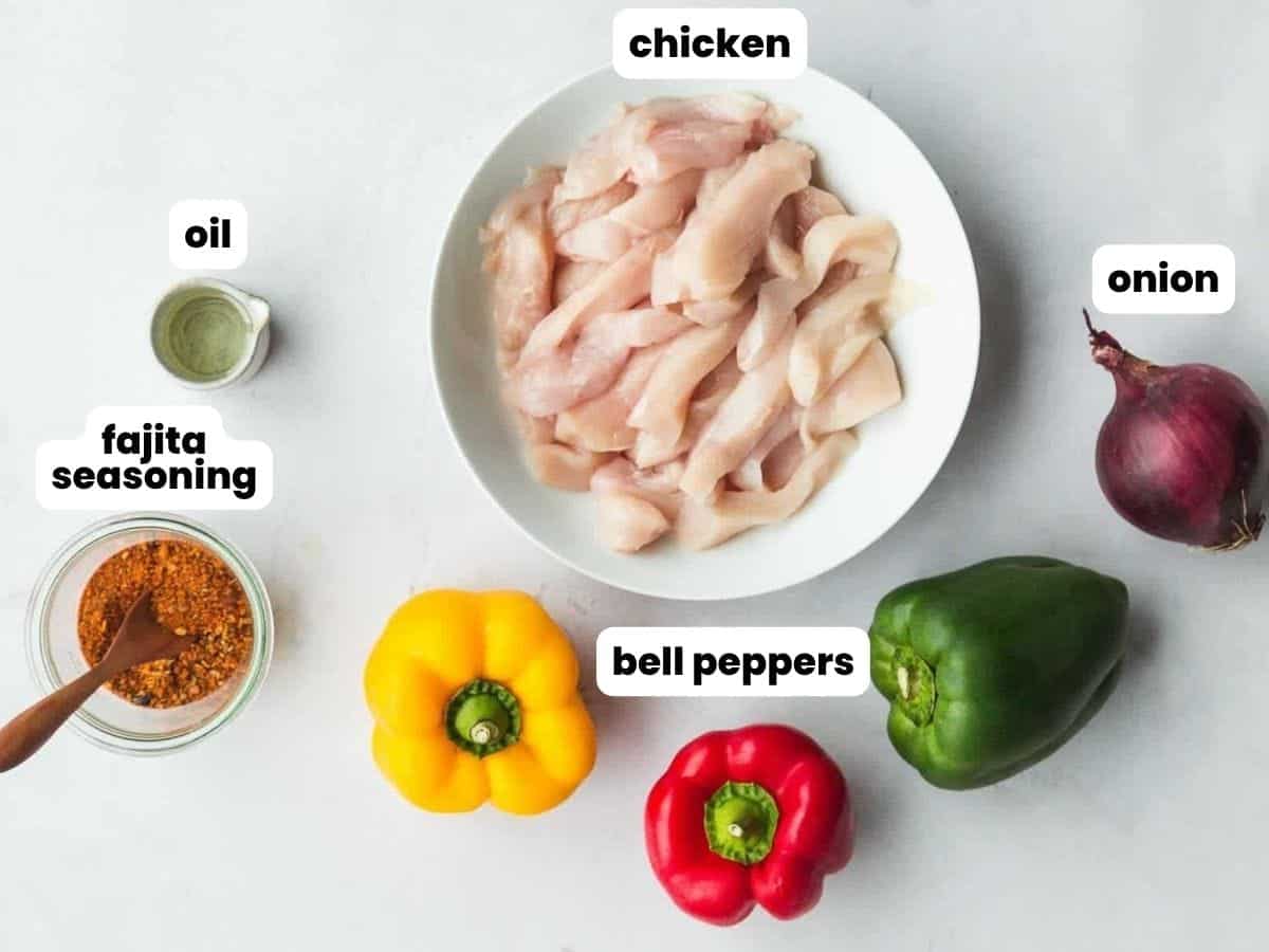 Overhead view of raw chicken strips on a plate with sliced bell peppers, a whole red onion, a small bowl of oil, and a bowl of fajita seasoning arranged on a light surface, with labels identifying each ingredient.
