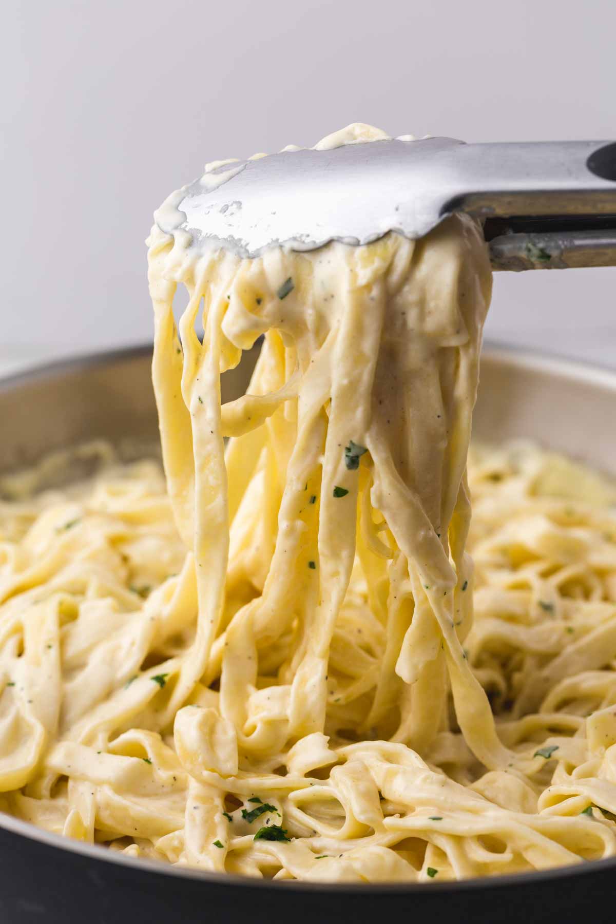 Serving creamy pasta with kitchen tongs