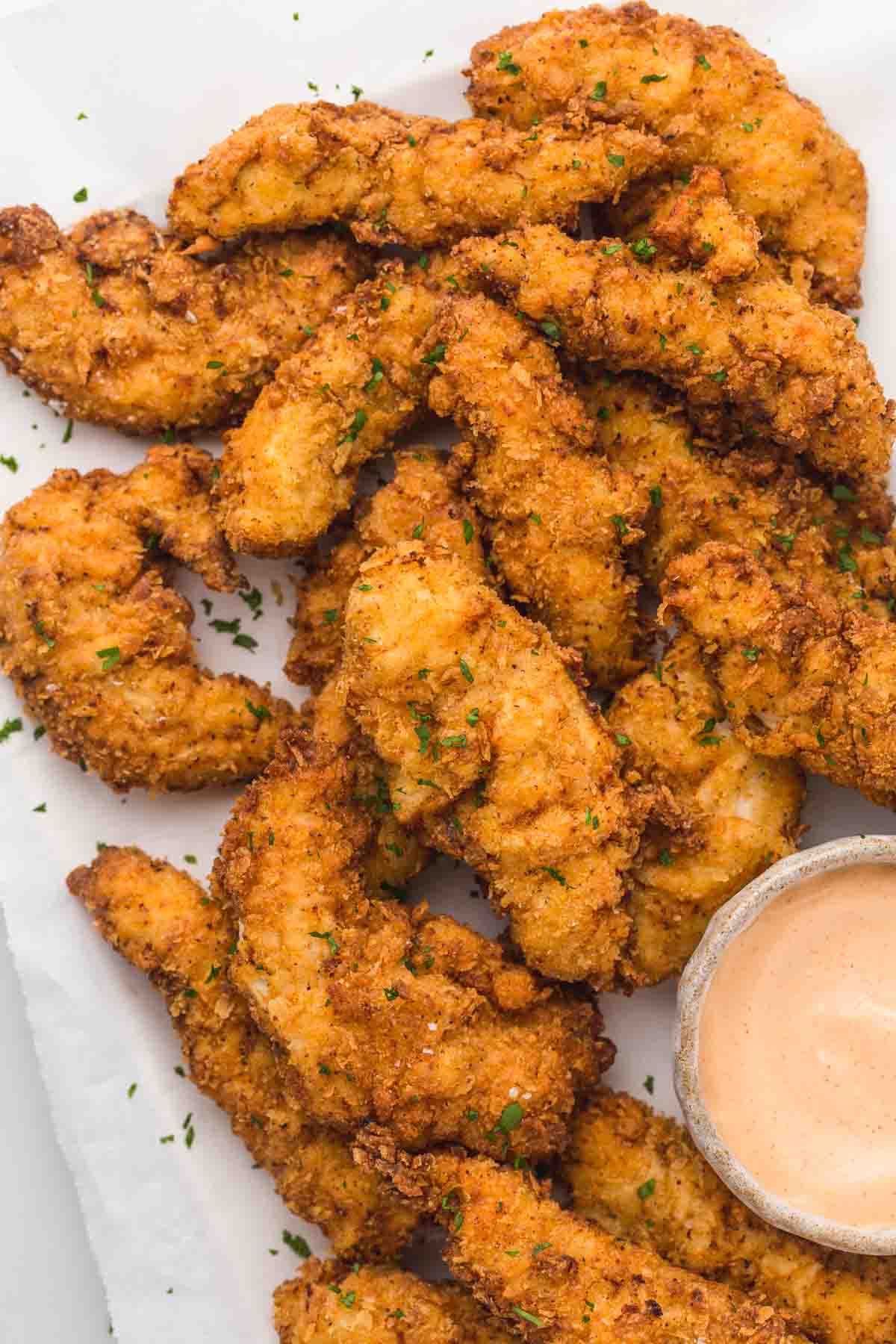 Overhead shot of golden brown chicken tenders and a dipping sauce.