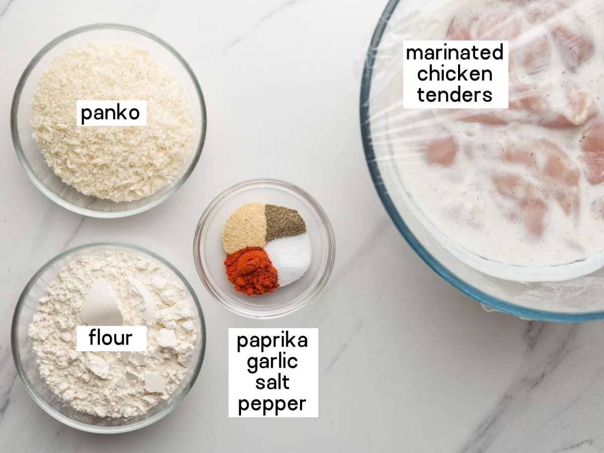 Ingredients needed to make buttermilk chicken tenders including tenders in buttermilk, flour, panko, and seasonings.