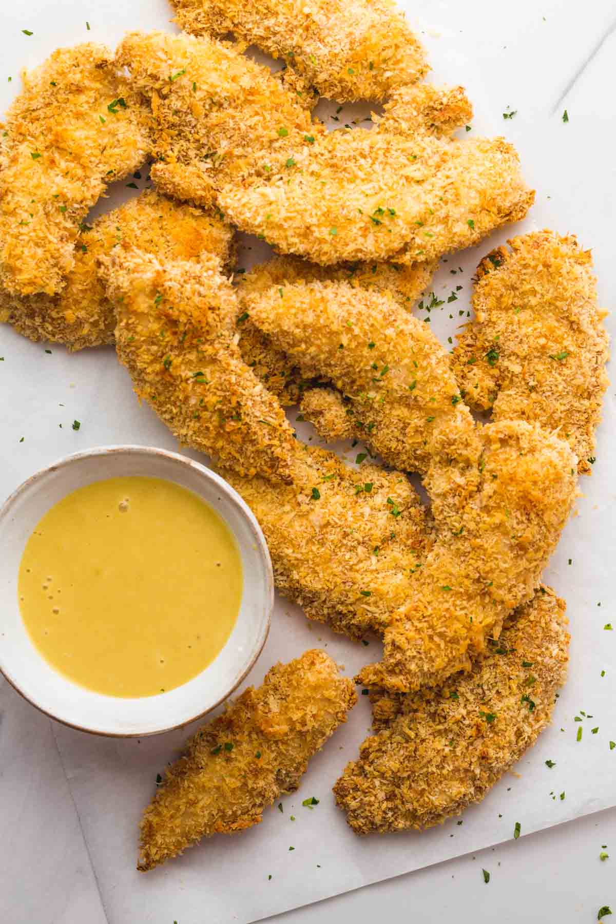 Crispy Oven Baked Chicken Tenders on parchment paper and honey mustard dip