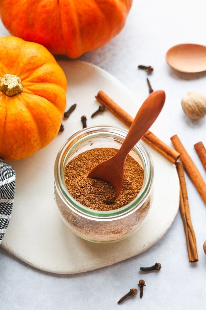 Pumpkin spice in a small Weck jar with a wooden spoon, and cinnamon sticks on the side.