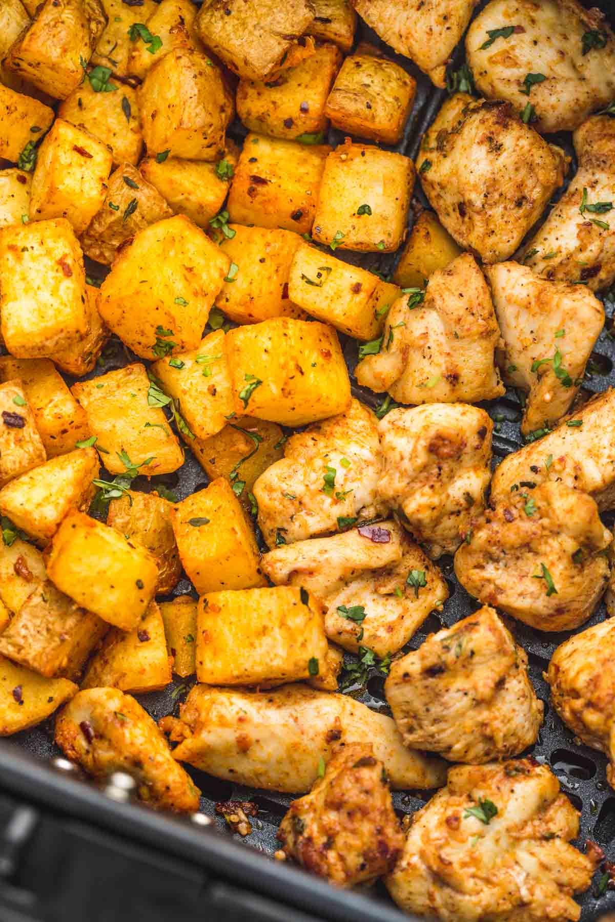 A close up of perfectly roasted potatoes, and cooked chicken pieces in an air fryer basket
