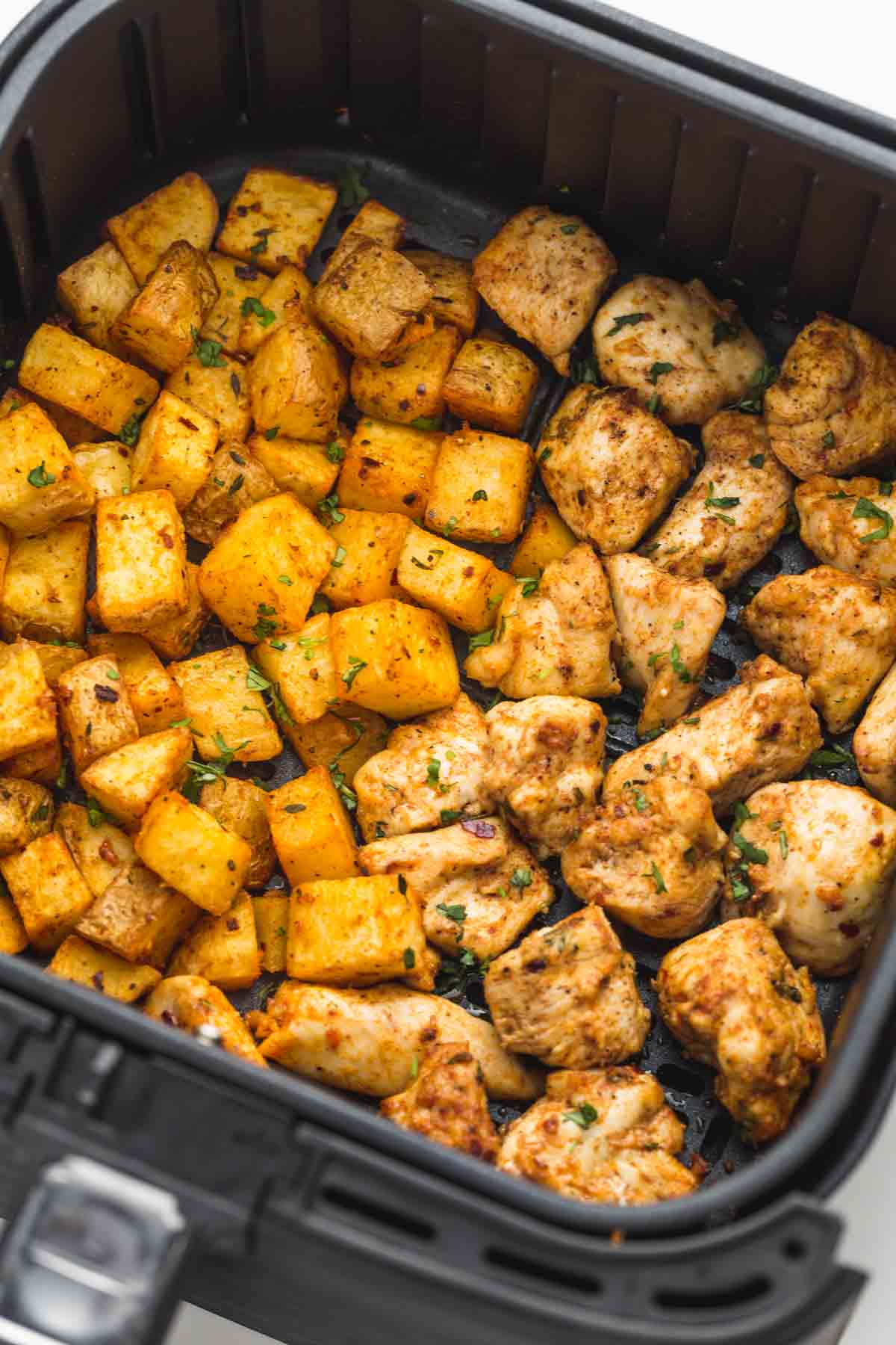 Roasted potatoes and chicken pieces in an air fryer basket