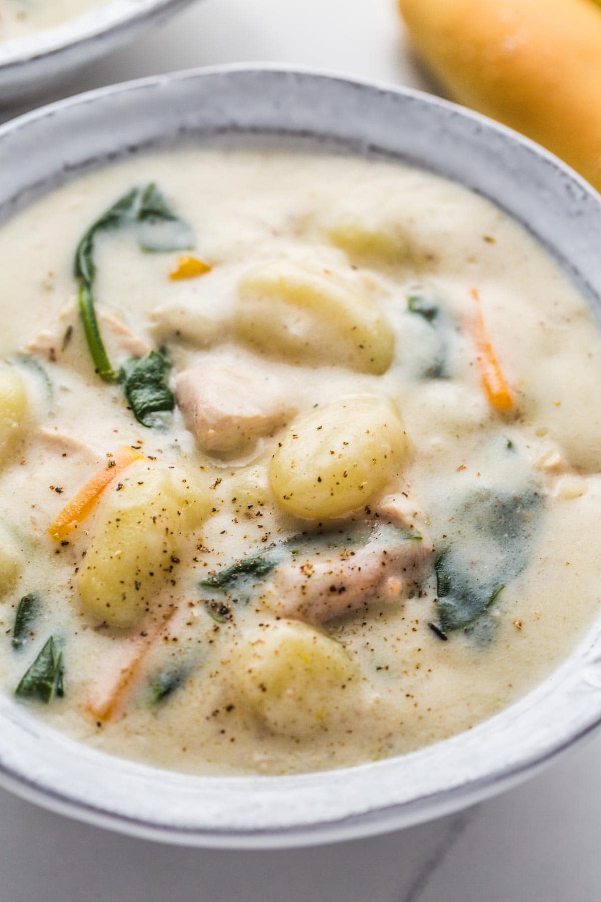 A close up of chicken gnocchi soup in a gray white bowl