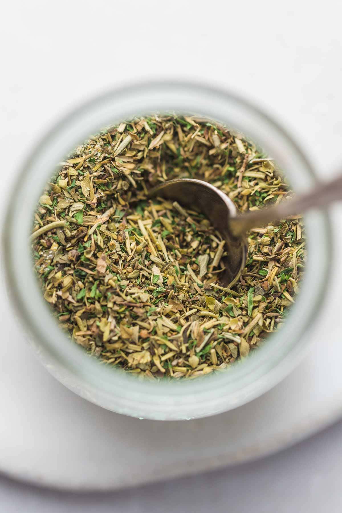 A close up of italian seasoning in a jar with a spoon