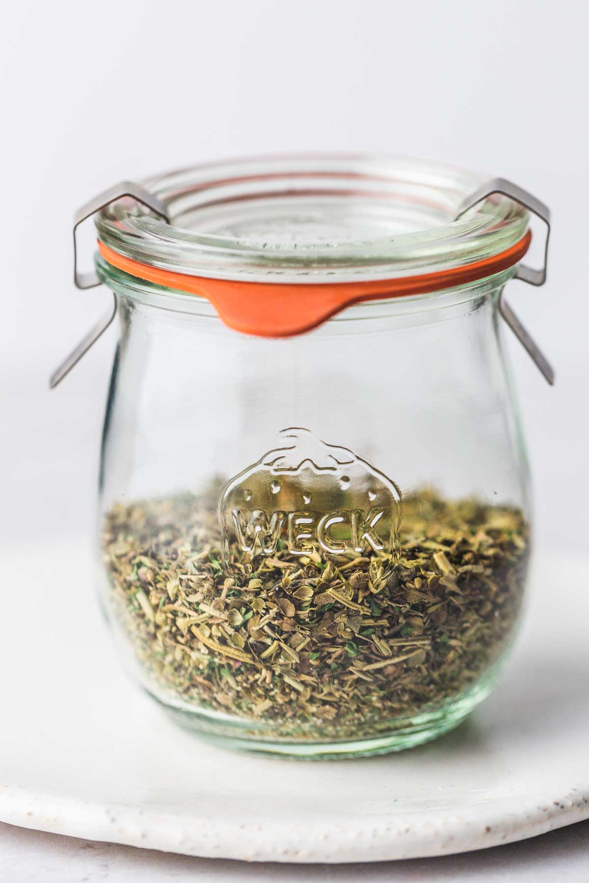 A small Weck jar with Italian seasoning, on a white plate