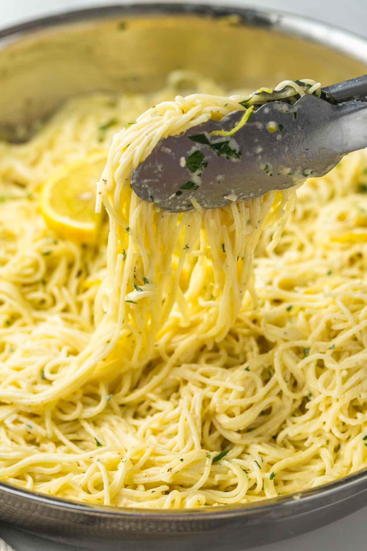Lemon pasta in a stainless steel skillet, serving pasta using kitchen tongs