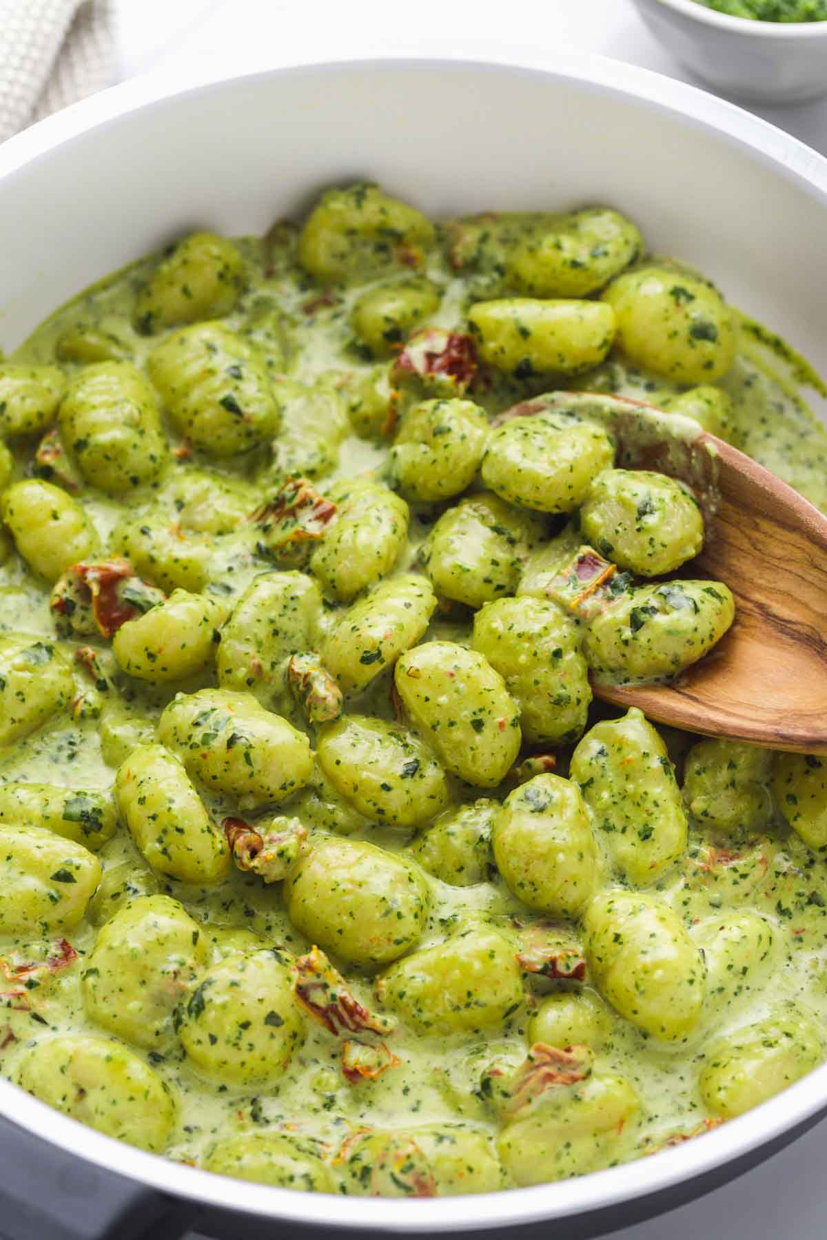 Close up shot of creamy gnocchi in sauce, and a wooden serving spoon.