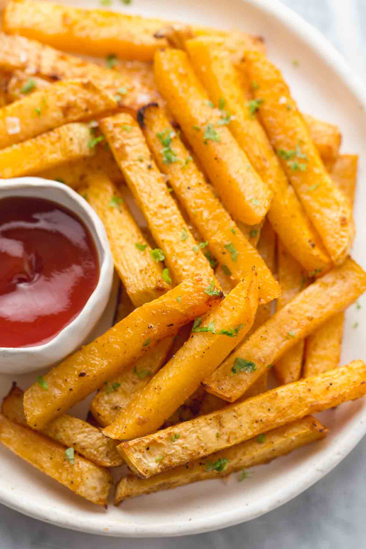 Golden rutabaga fries served on a white plate with ketchup