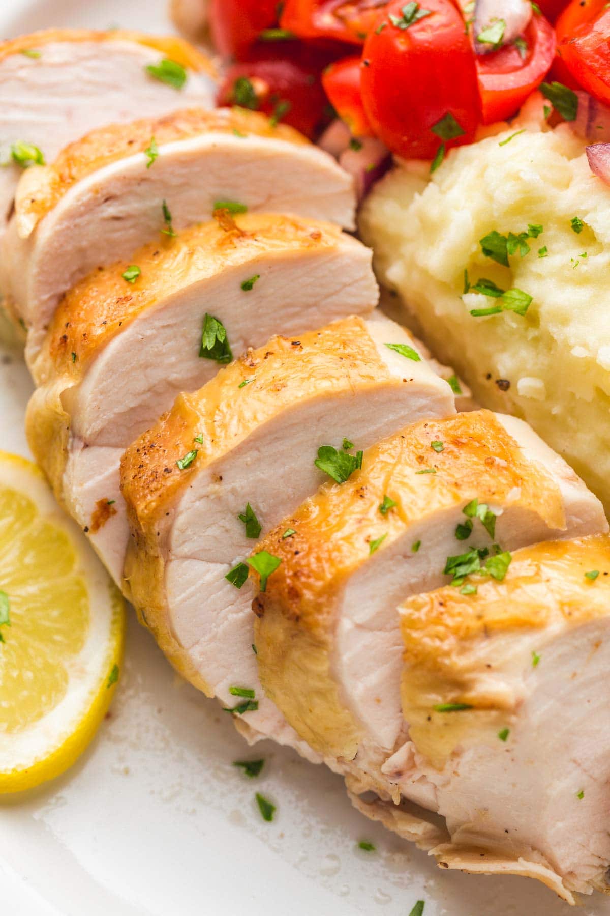 Sliced chicken breast with mashed potatoes and lemon slices.