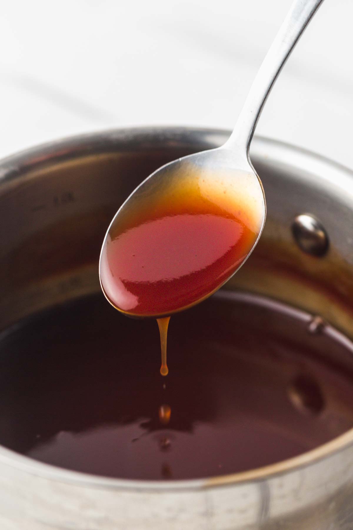 A spoon with Sweet and Sour Sauce over a saucepan