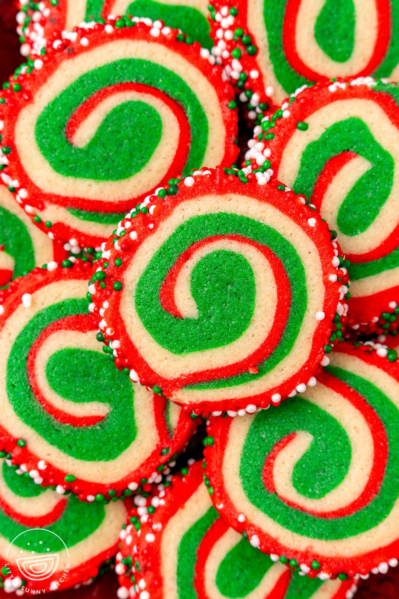 Close-up of a festive batch of Christmas pinwheel cookies featuring red, green, and white swirls, coated with red, green, and white sprinkles.