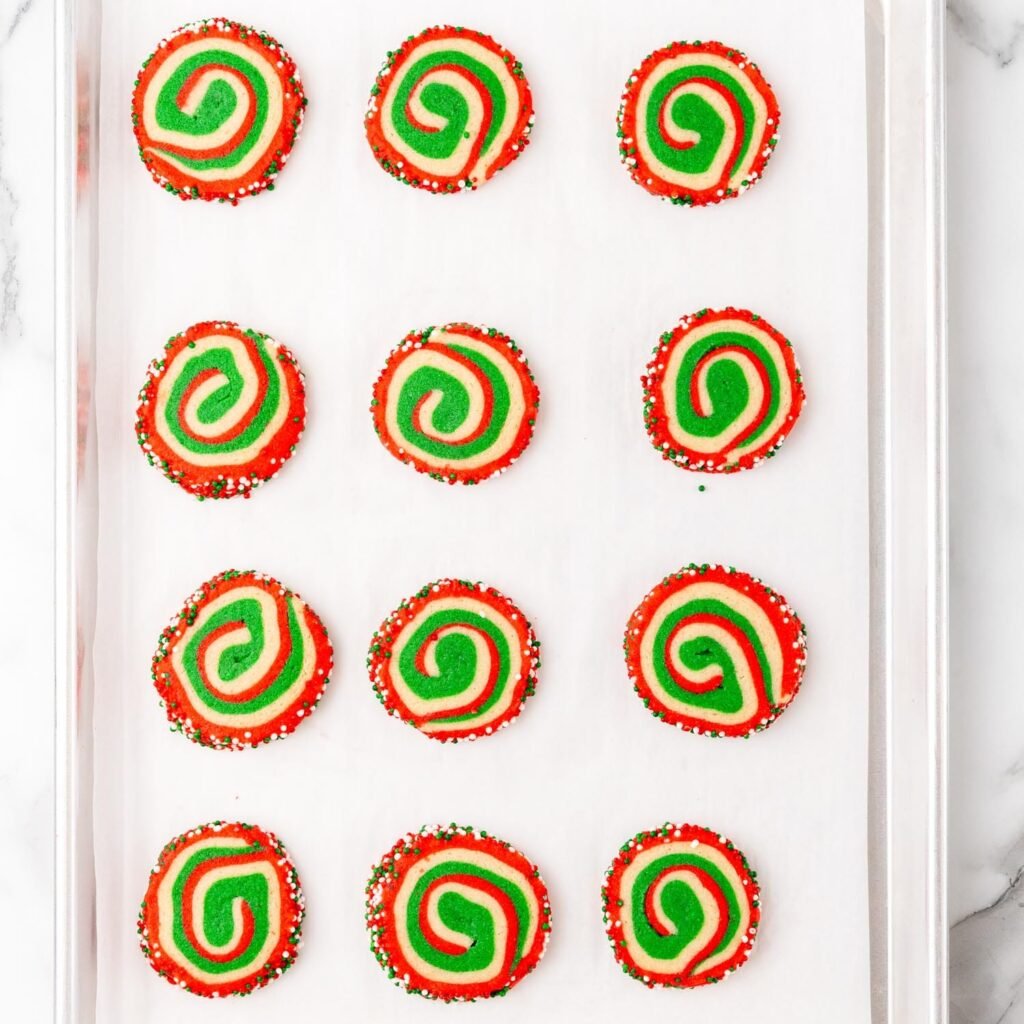 Baked Christmas pinwheel cookies on a parchment-lined baking sheet, showing vibrant red, green, and white swirls.