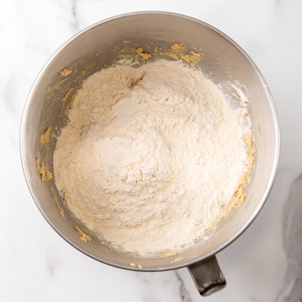 A mixing bowl containing the dry ingredients (flour, baking powder, and salt) added to the wet mixture of butter, sugars, egg, and vanilla, ready to be combined for Christmas pinwheel cookie dough.