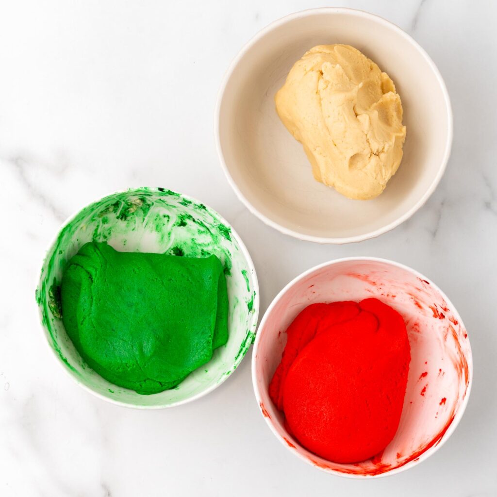 Three bowls of dough: one plain, one colored green, and one colored red, ready for layering to make Christmas pinwheel cookies.