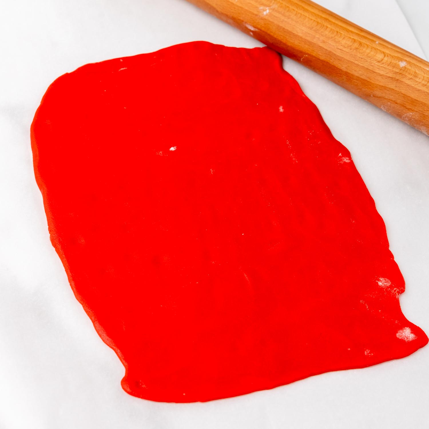 Rolled-out red dough on parchment paper with a rolling pin nearby, ready to be layered for Christmas pinwheel cookies.