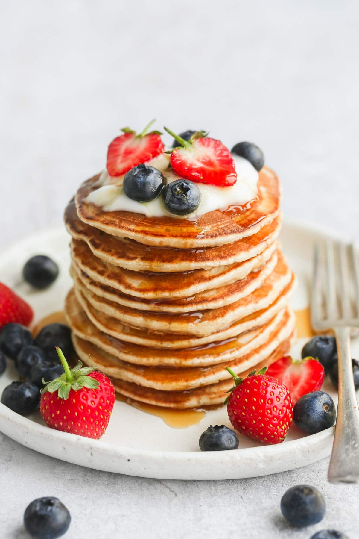 A stack of pancakes on a white plate with fresh fruit