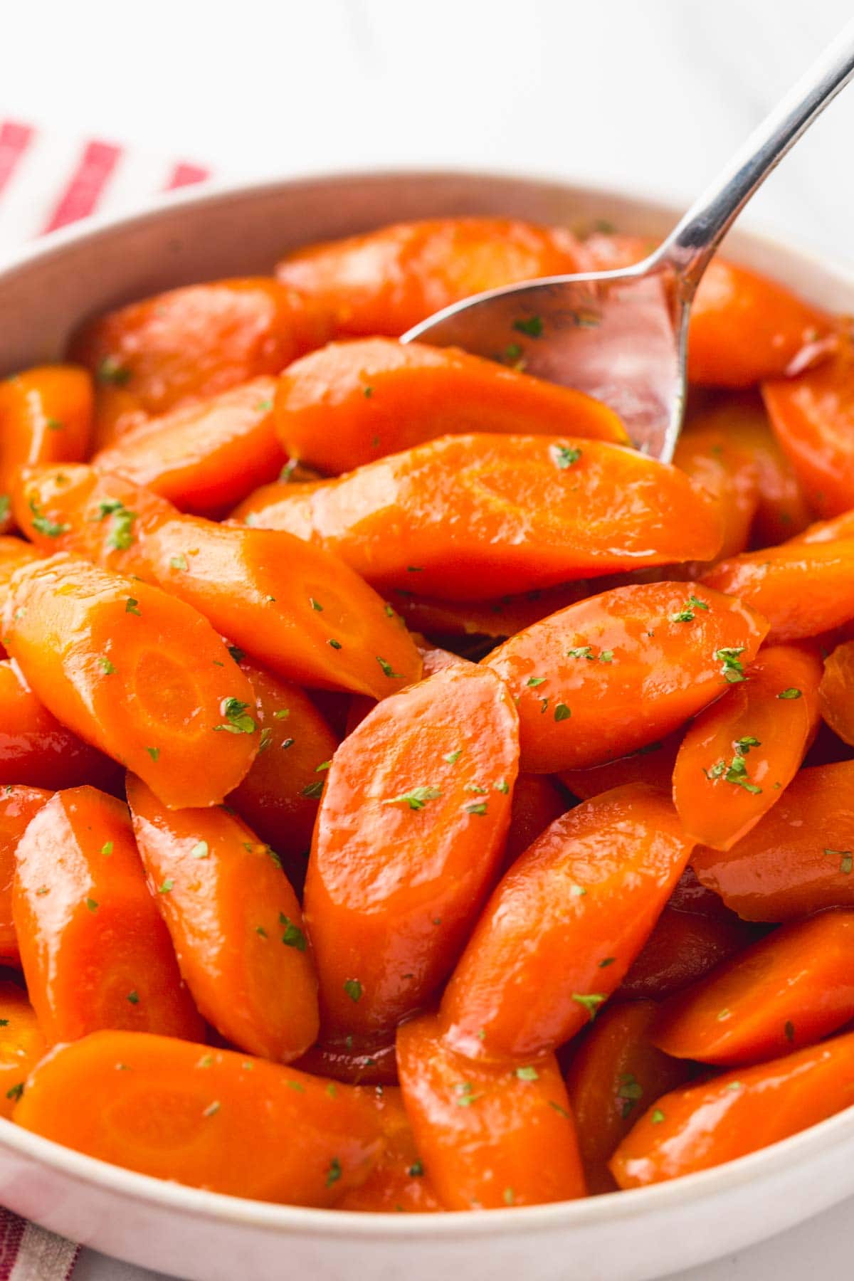 Glazed carrots in a large white bowl with a serving spoon