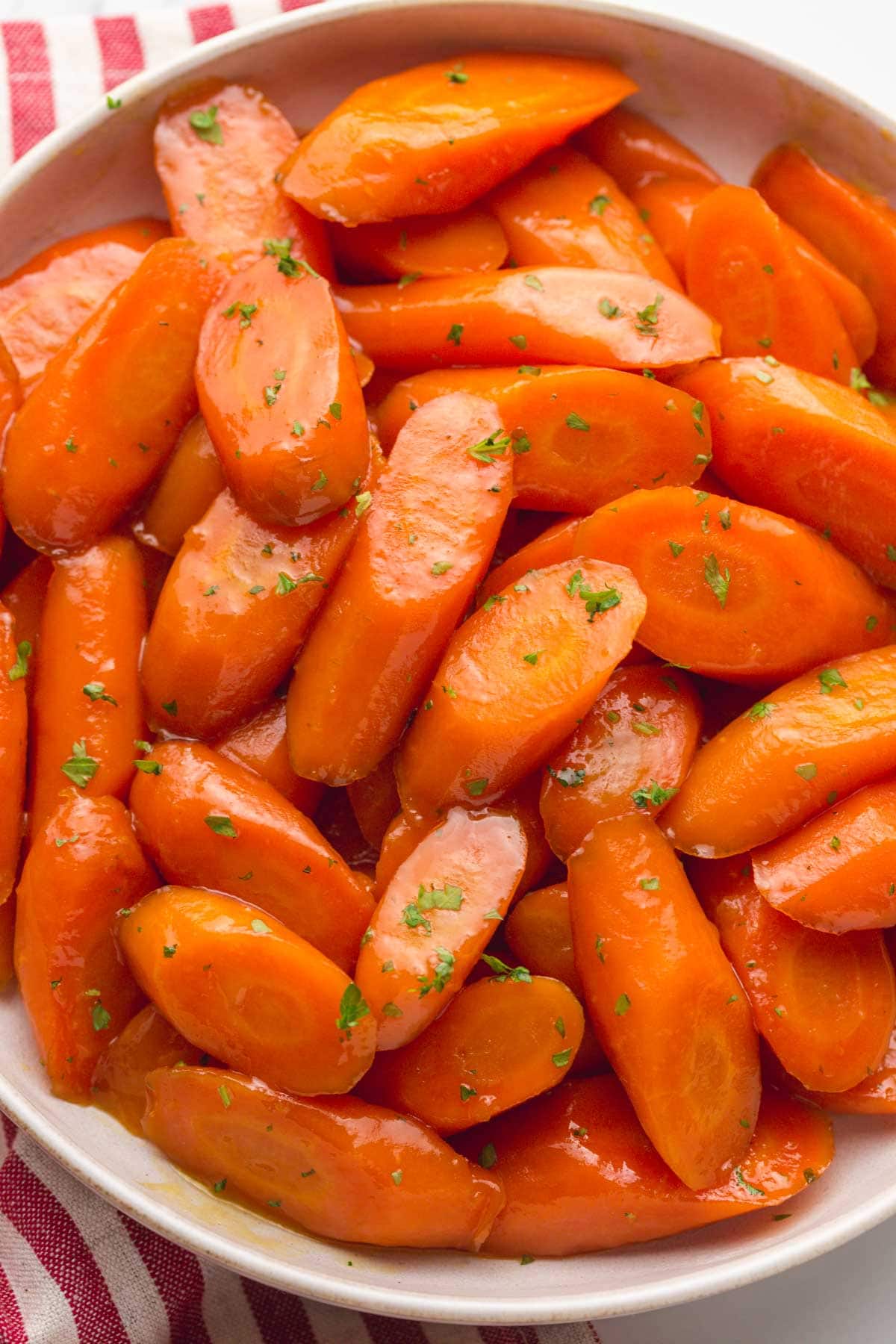 An overhead shot of glazed carrots in a white bowl, garnished with fresh chopped parsley.