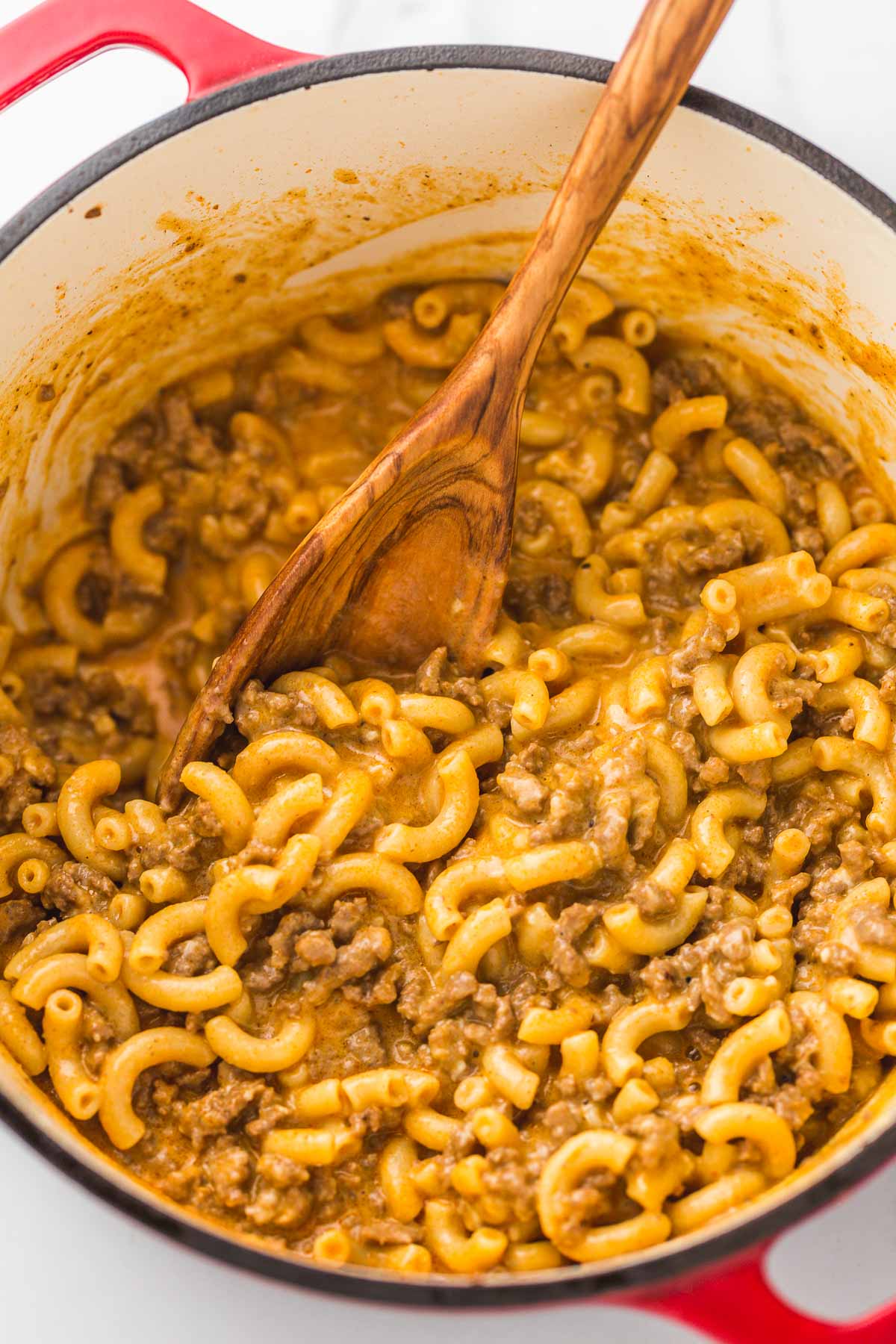 Hamburger helper recipe in a large red dutch oven, and a wooden spoon.
