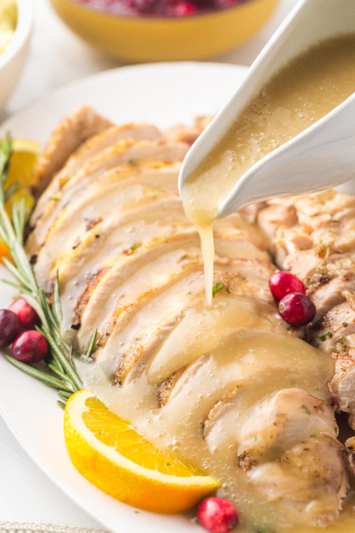 Sliced turkey breast on a platter with gravy being poured from a gravy boat