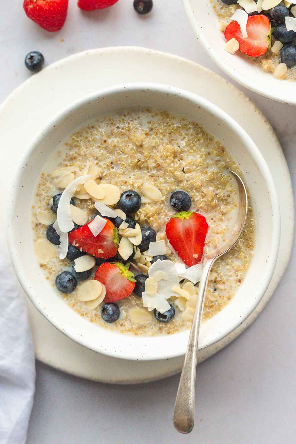 A white bowl of quinoa porridge with fresh fruit and a large spoon