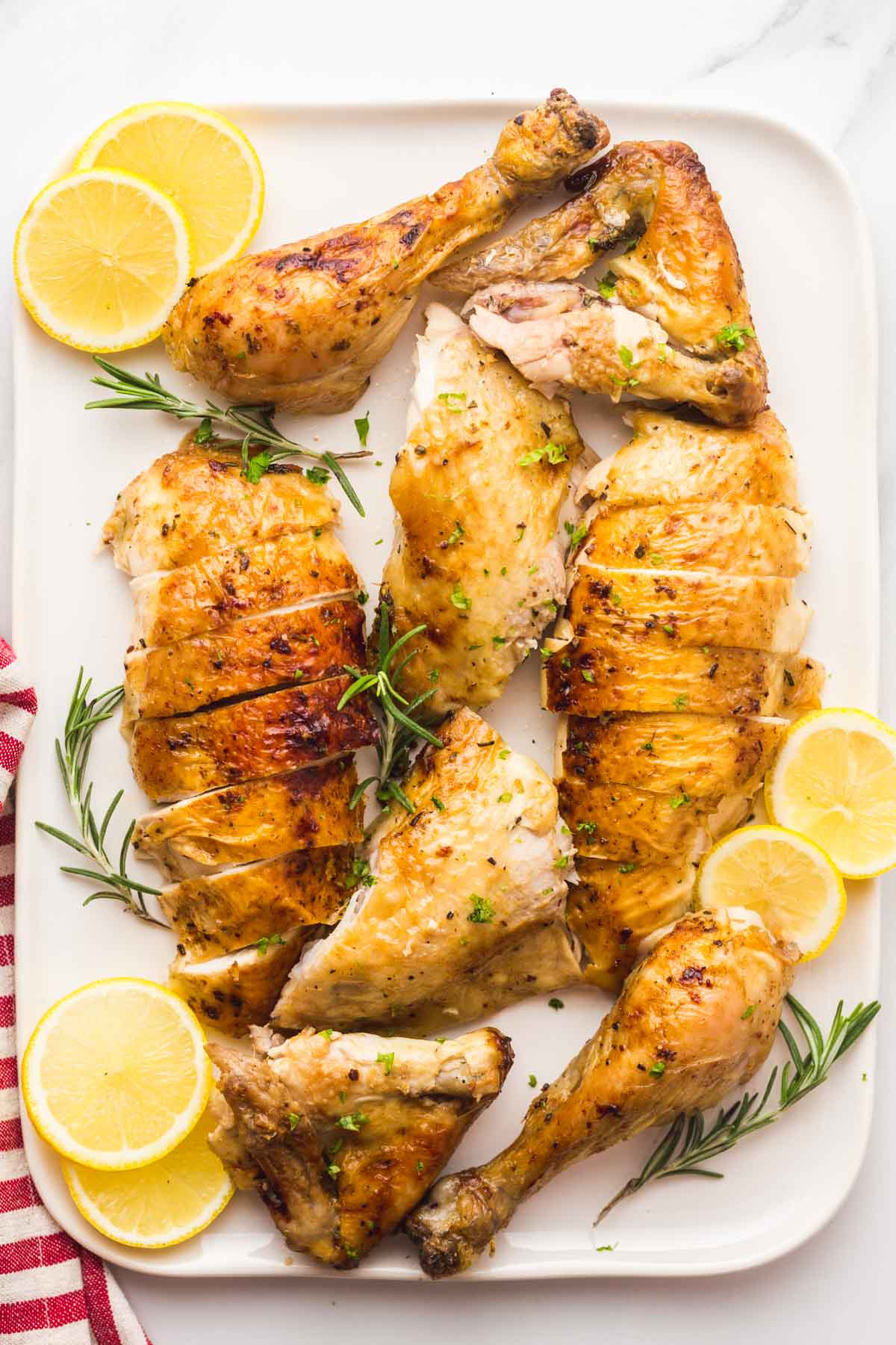 Carved chicken on a white platter with lemon slices and fresh rosemary sprigs.