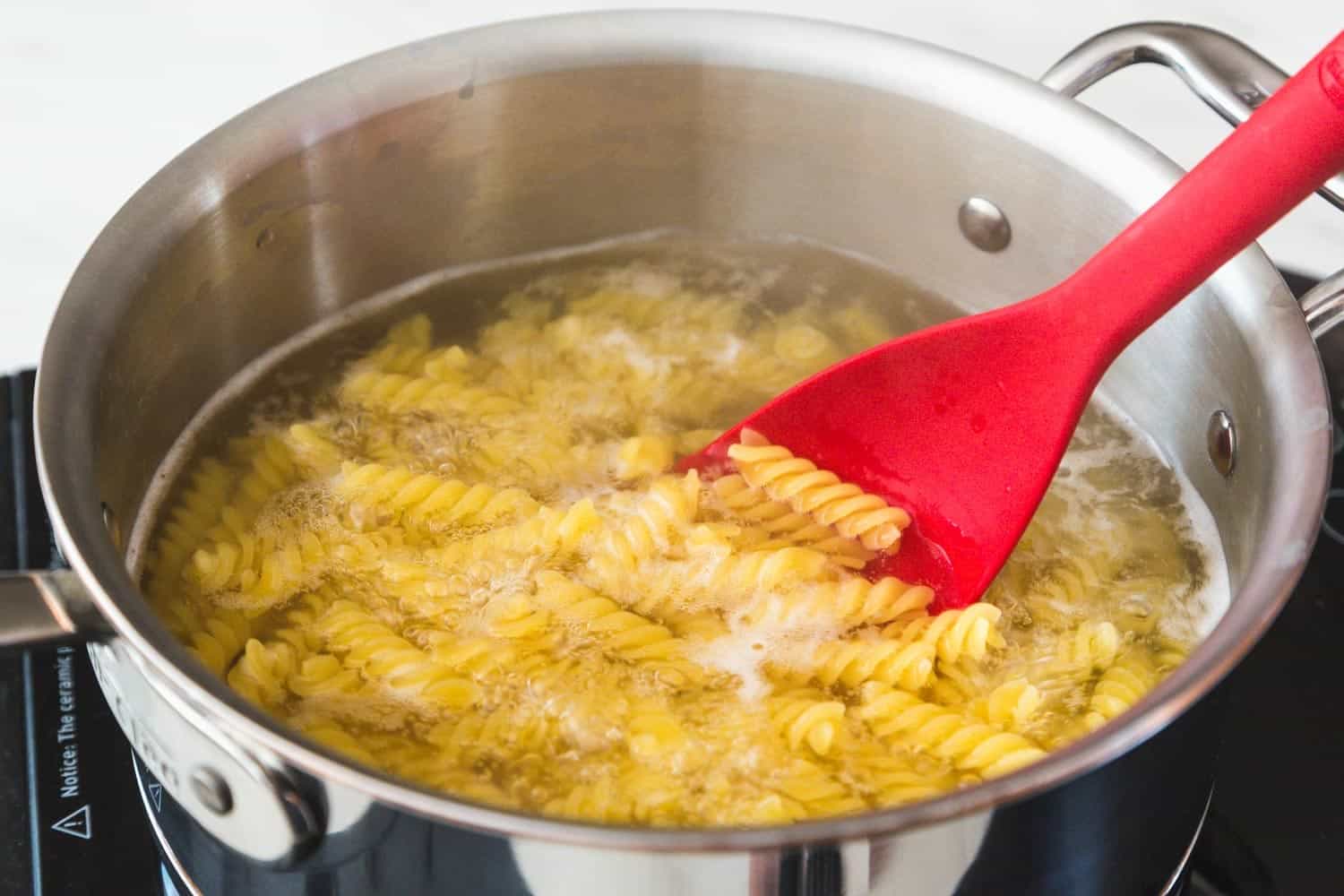 Cooking pasta in a saucepan, and a red spatula stirring the pasta