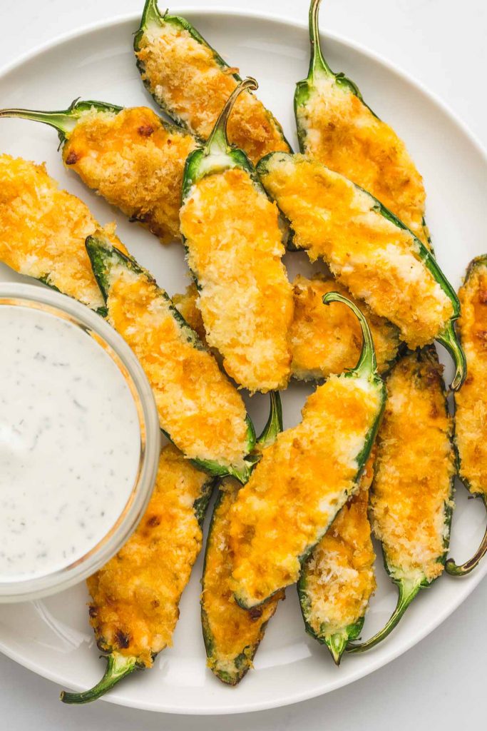 Jalapeno poppers served on a white plate with a dip