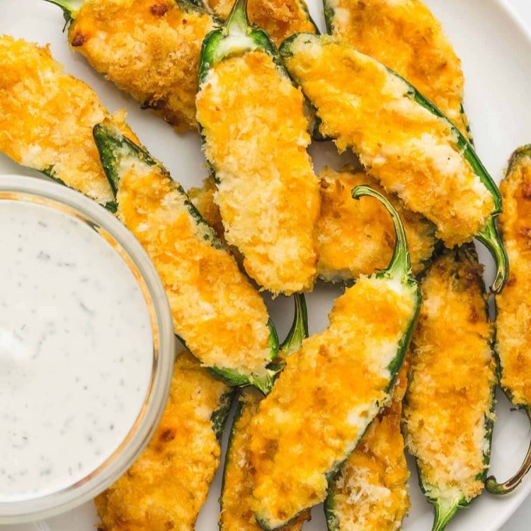 Jalapeno poppers served on a white plate with a dip
