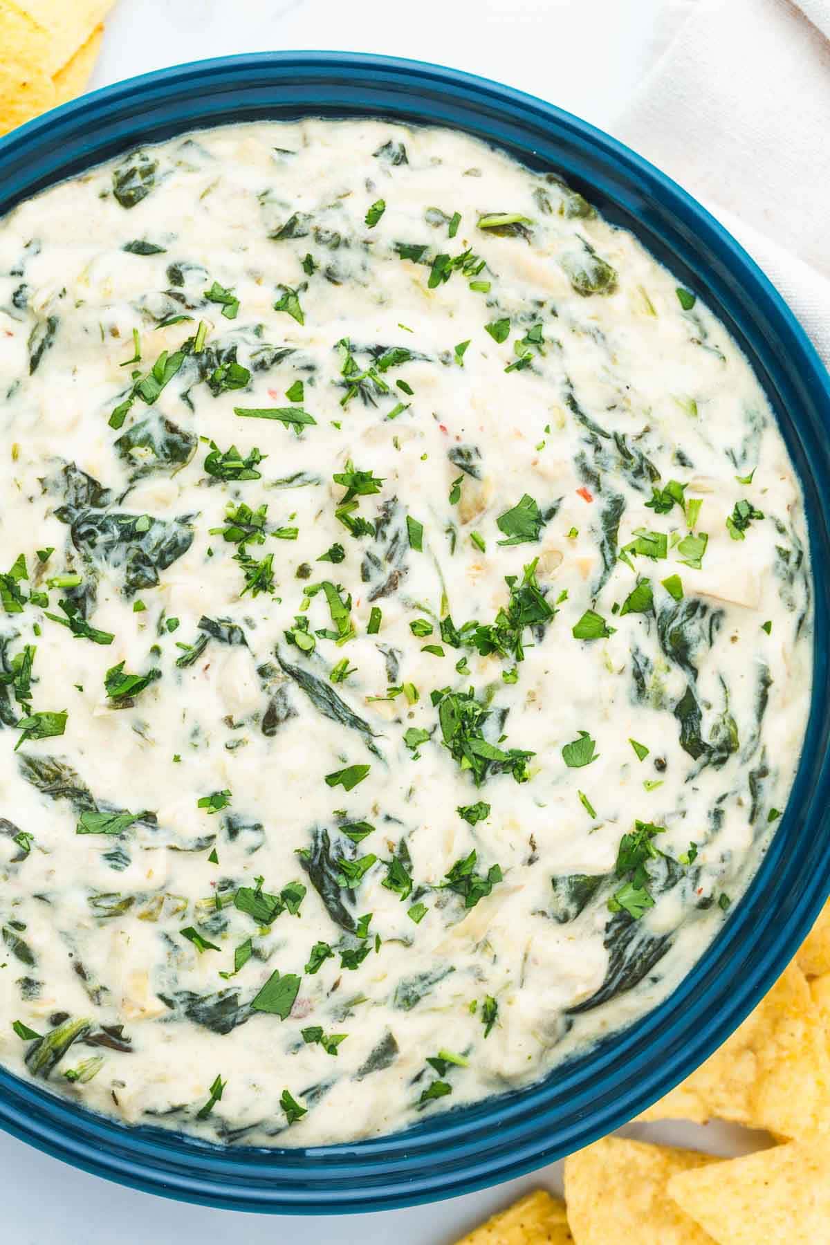 Overhead shot of a bowl of spinach artichoke dip, with corn tortilla chips on the side.