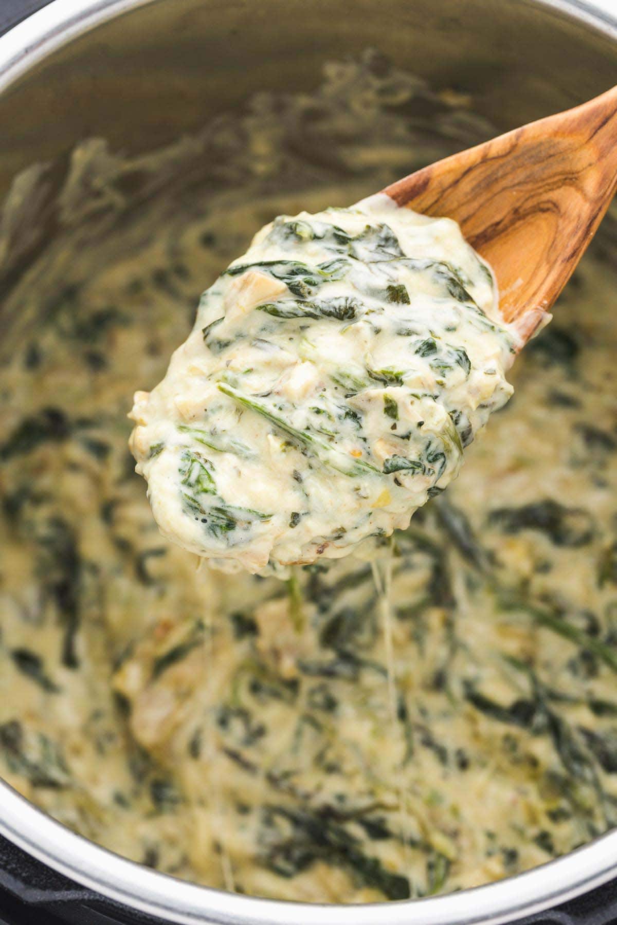 A serving wooden spoon with spinach artichoke dip