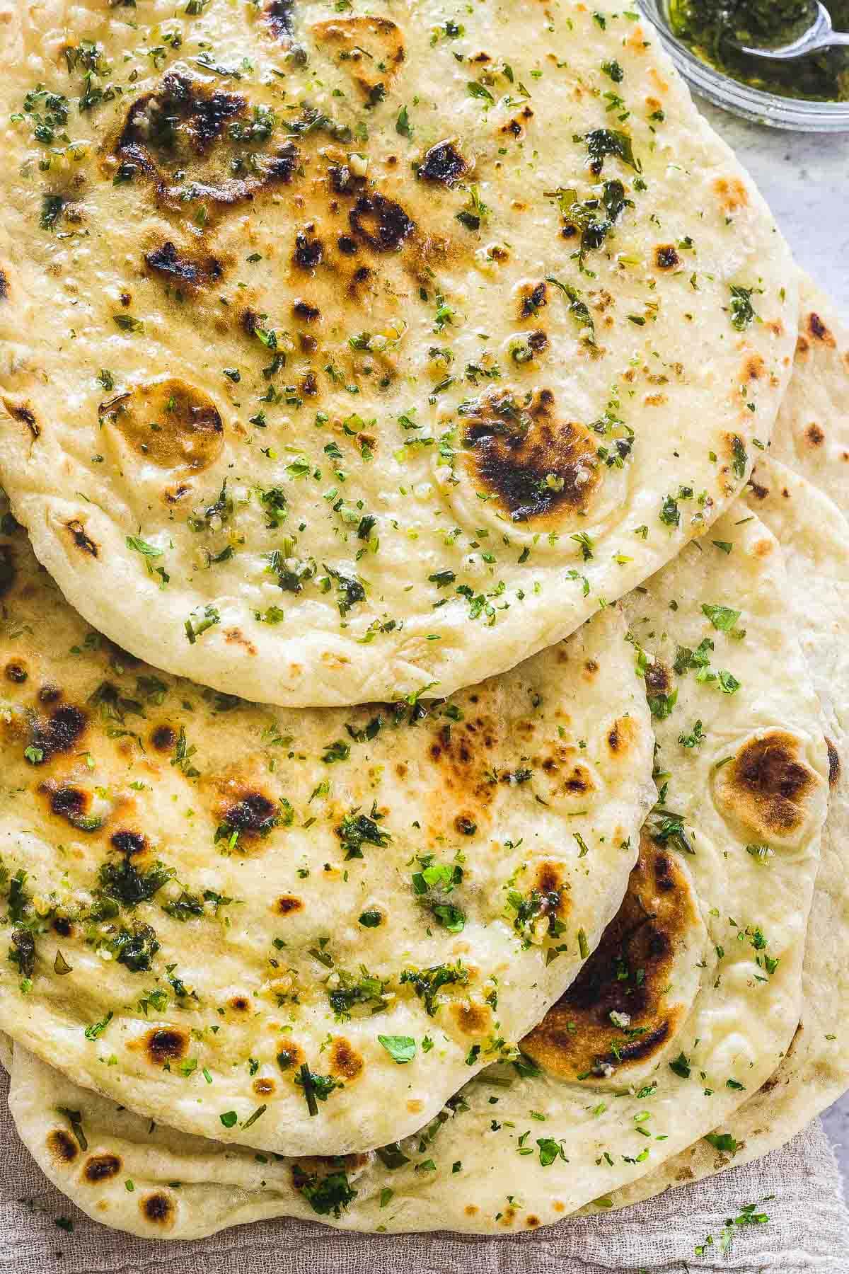 A close up of homemade naan bread stacked on each other, and brushed with herb garlic butter.