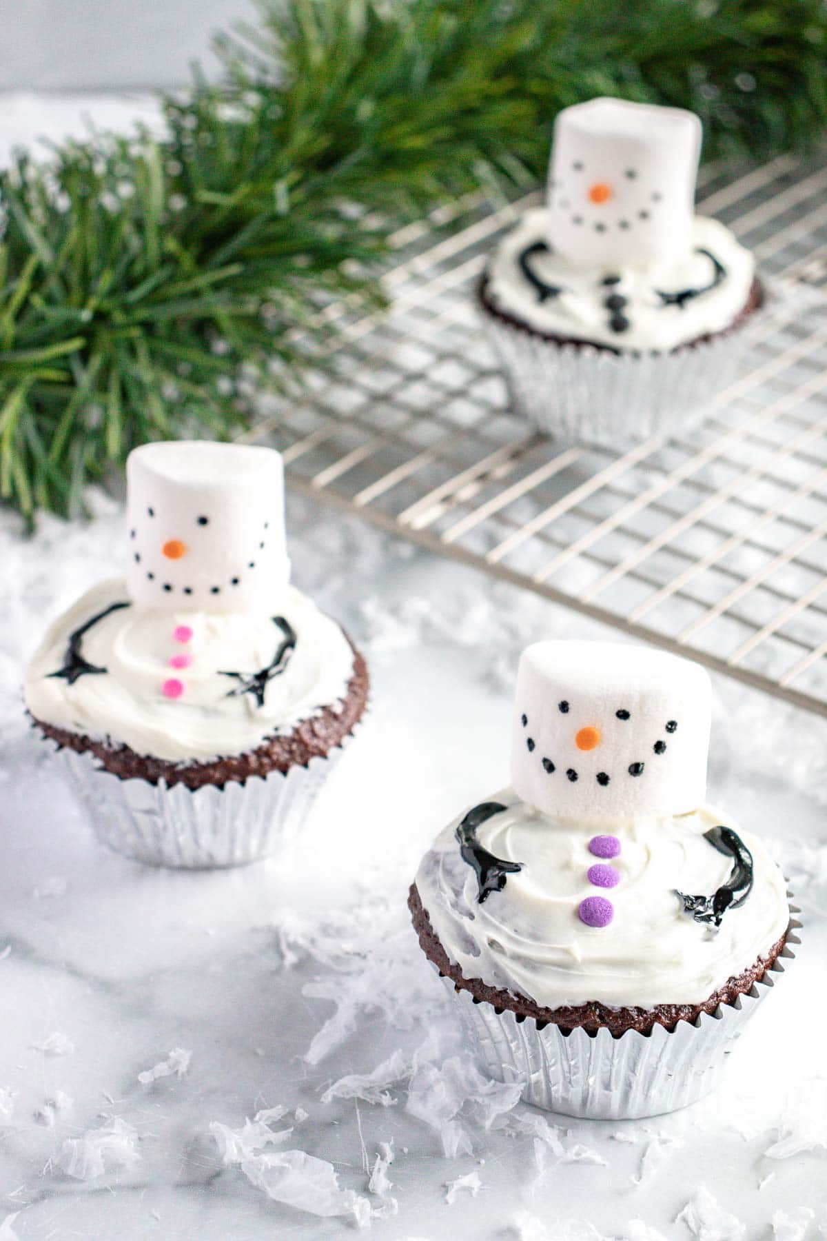 3 snowman cupcakes on a marble countertop