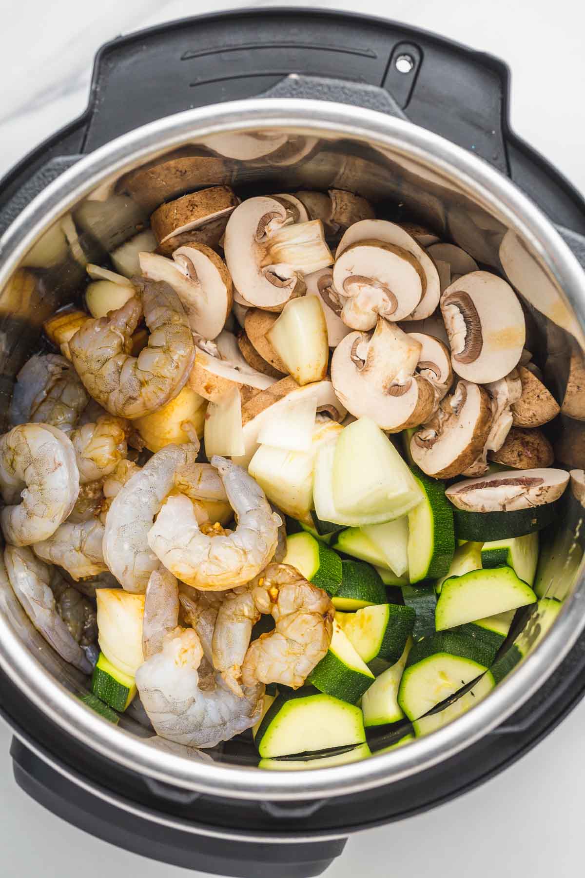 The ingredients in the Instant Pot. Raw thawed shrimp, sliced zucchini, onion, mushrooms.
