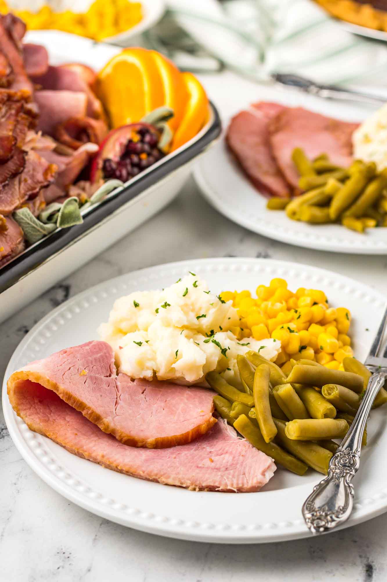 Plated slice of honey glazed ham with green beans, mashed potatoes, and corn.