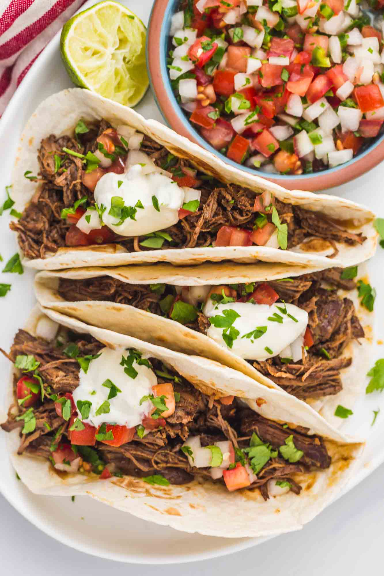 Overhead shot of shredded beef tacos with pico de gallo and lime crema