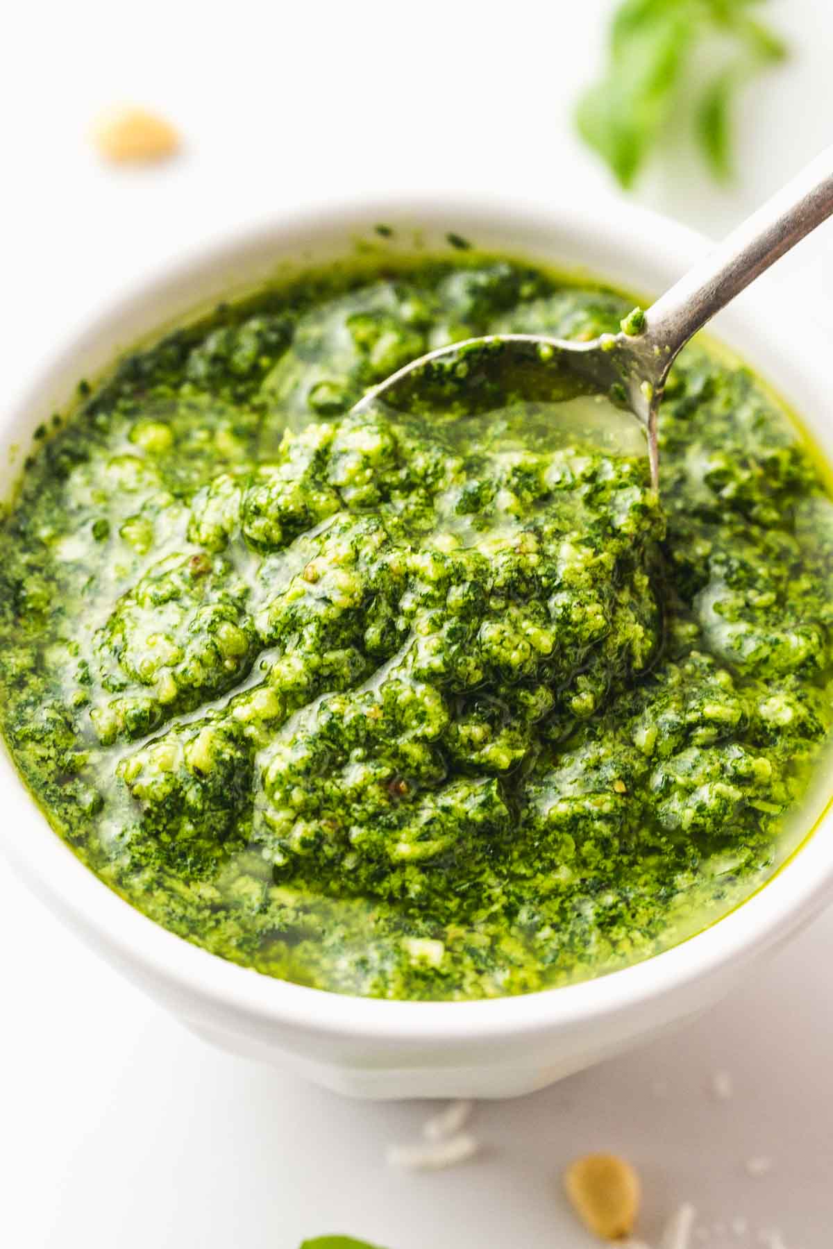 A white bowl with basil pesto and a small teaspoon